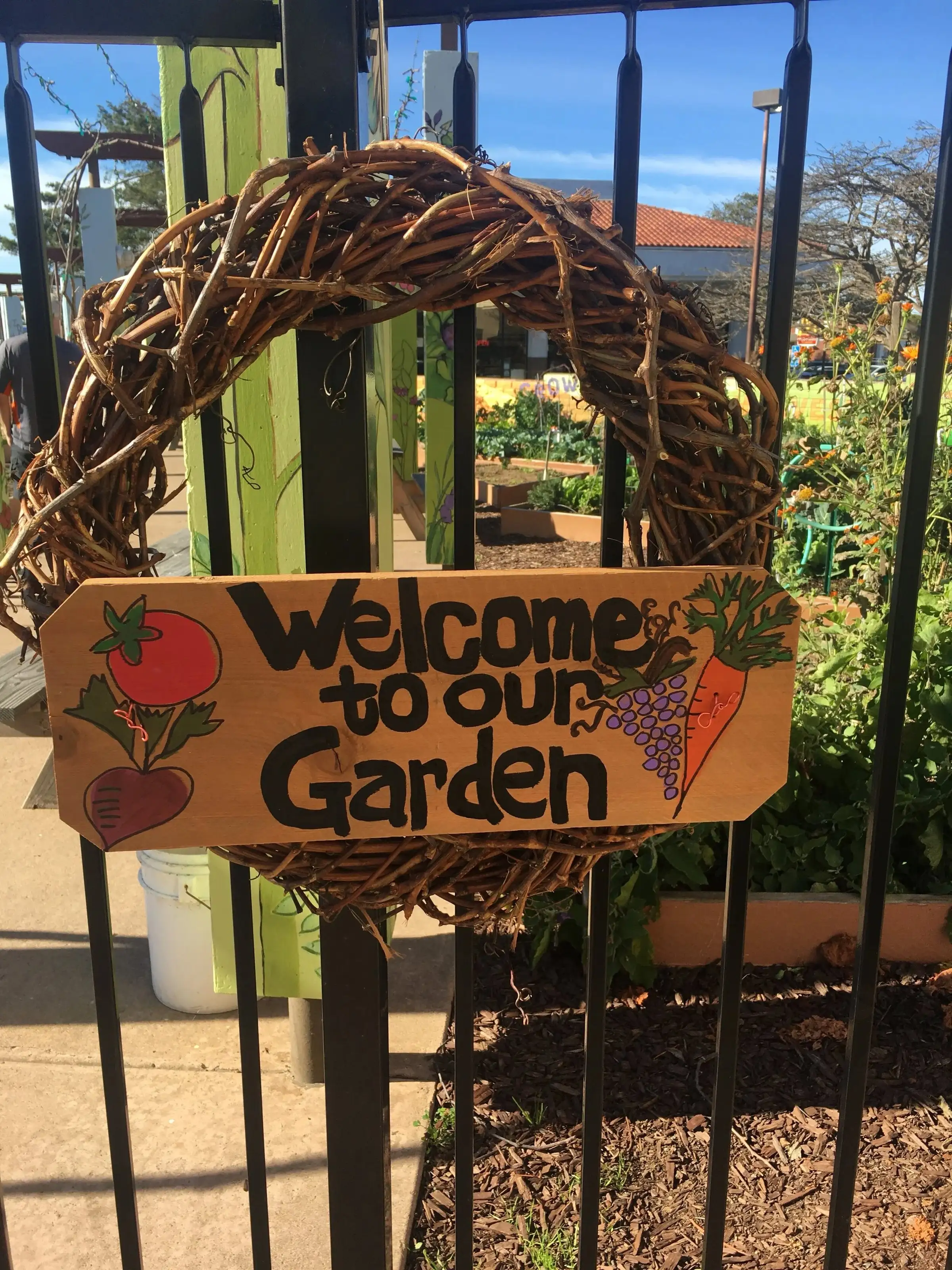 A hand-painted “Welcome to our Garden” sign framed by a grapevine wreath on the garden gate
